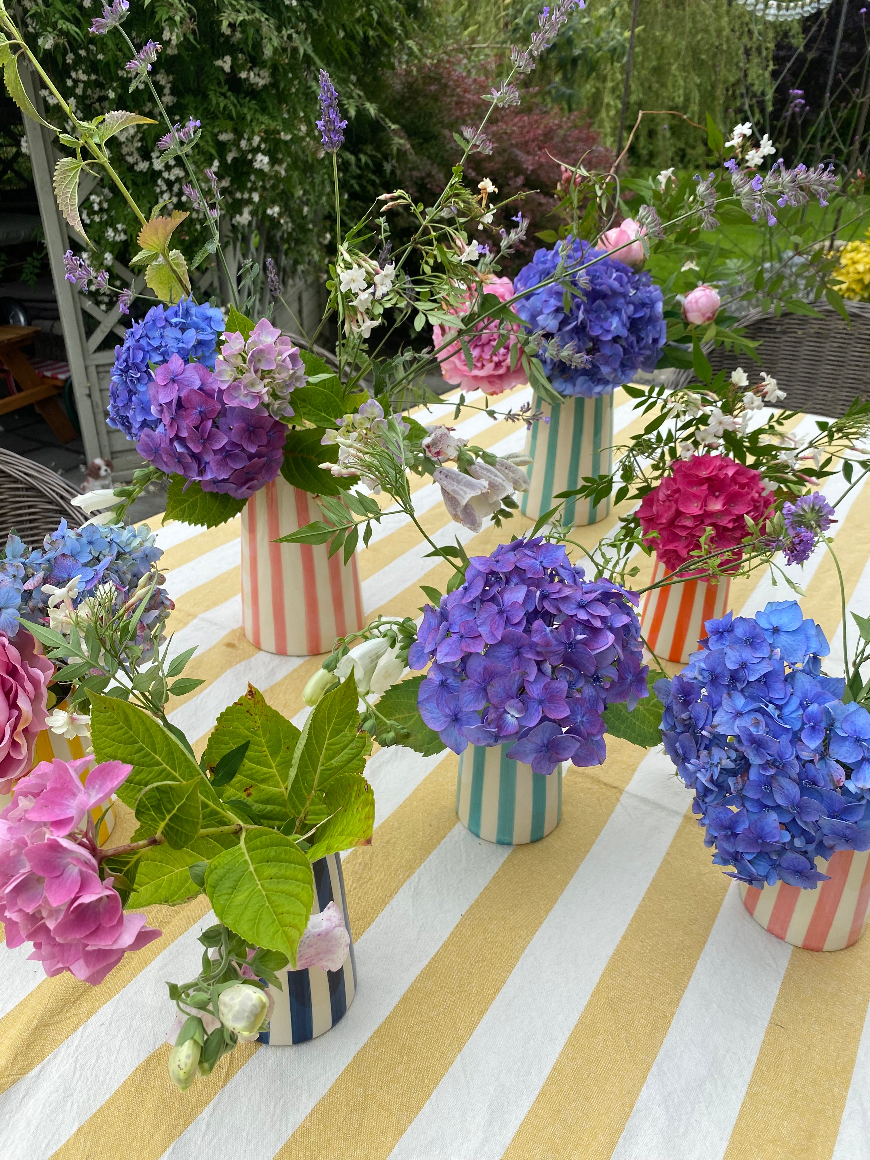 cluster of colourful striped jugs on outdoor table with yellow and white stripes