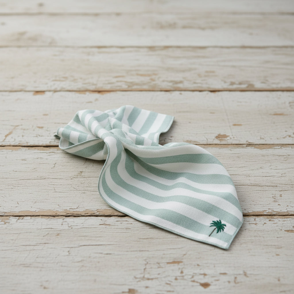 A striped napkin with a palm tree embroidery detail on a table setting, with a striped tablecloth and purple glasses in the background.