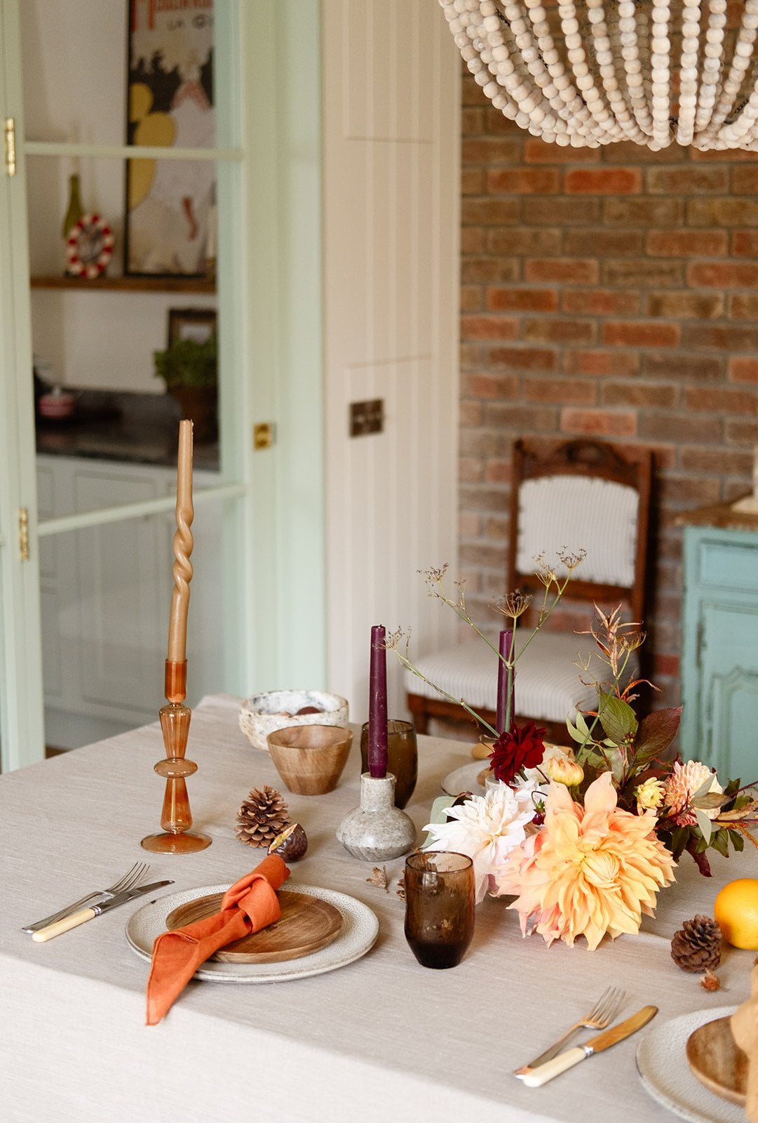 Nature-inspired table setting with brick wall and green crittall doors, linen table cloth, brown glasses, rust coloured candle holders