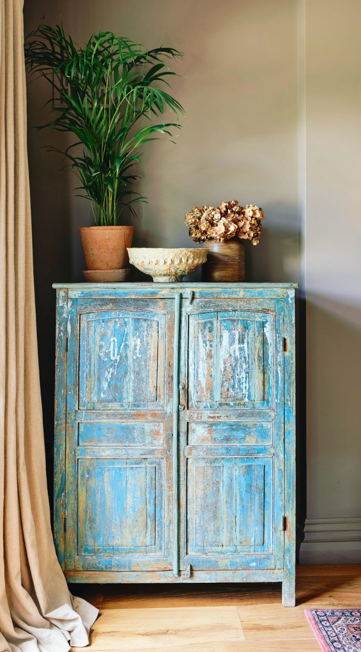 Vintage-style blue cabinet with decorative items against a neutral wall.