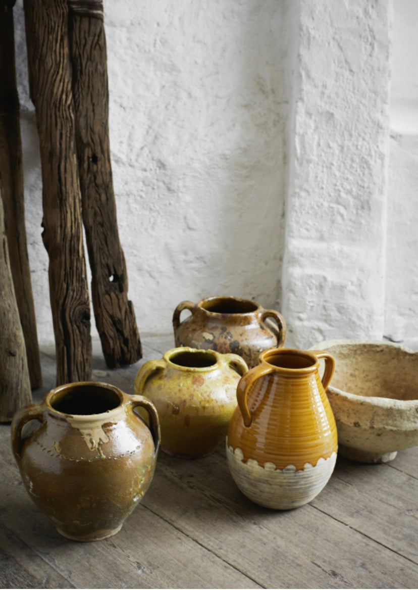 Collection of vintage stoneware vessels and pots on an old wood floor in front of a textured white wall