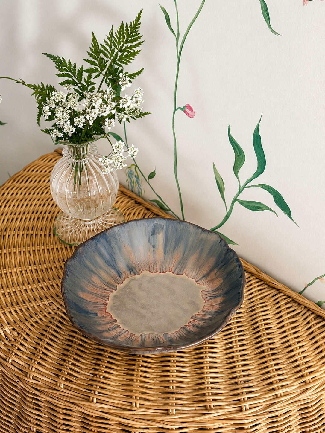 Watercolour footed bowl on rattan table next to glass vase of green flowers in front of a hand painted mural