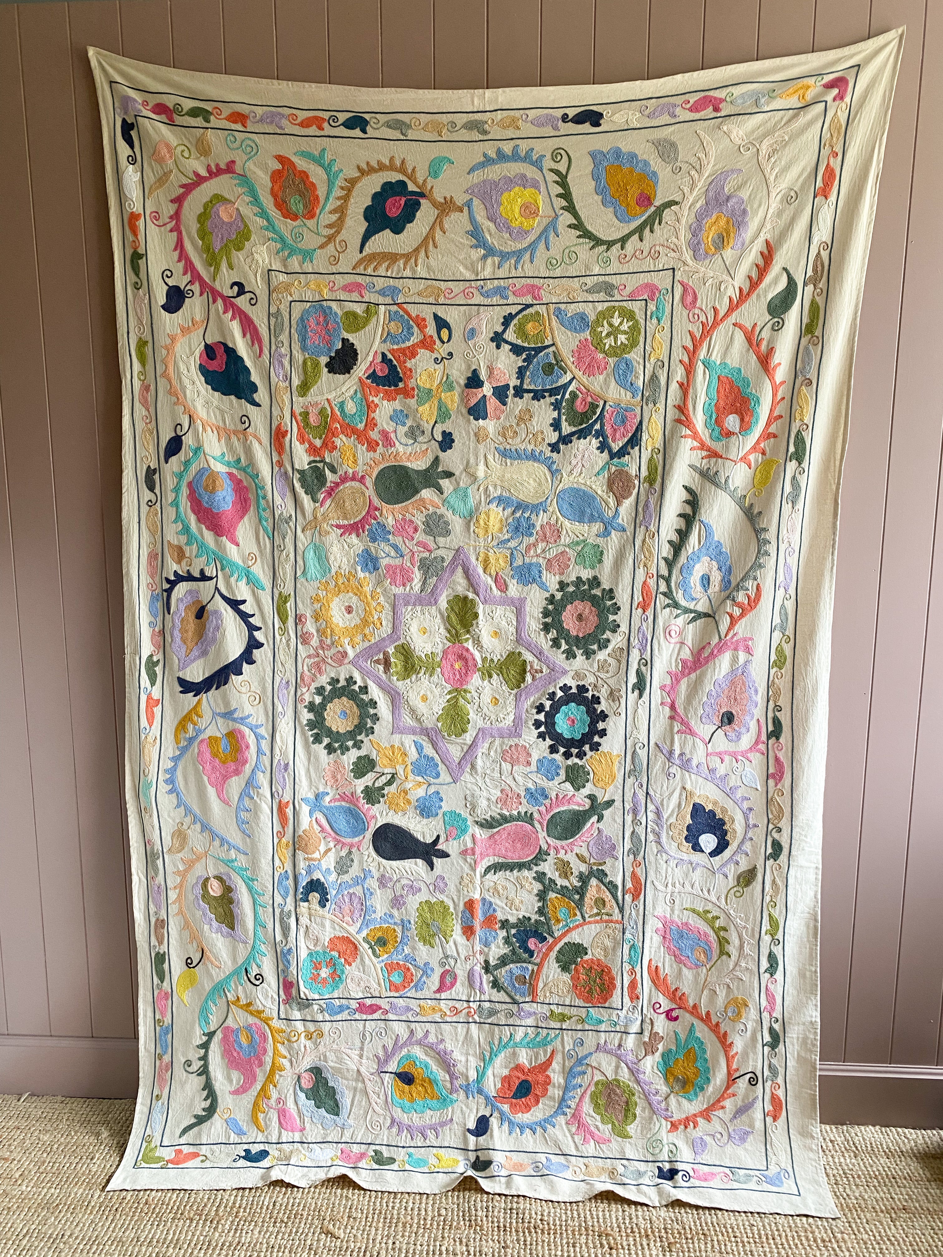 A vintage suzani featuring intricate floral and vine motifs with natural dyes, hand-embroidered on a cotton sheet.