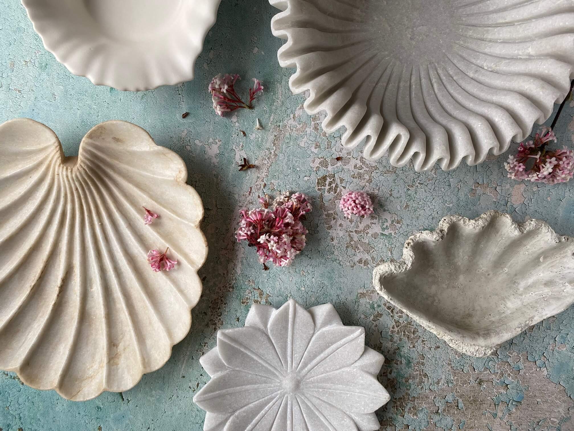 Aerial view of a collection of white decorative bowls in different sizes, shapes, textures and materials against blue textured background