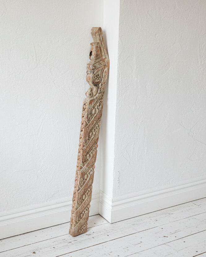 A reclaimed indian wood panel with metal hooks, standing upright on an old white wooden floor against a textured white wall, showing signs of natural texture and color.