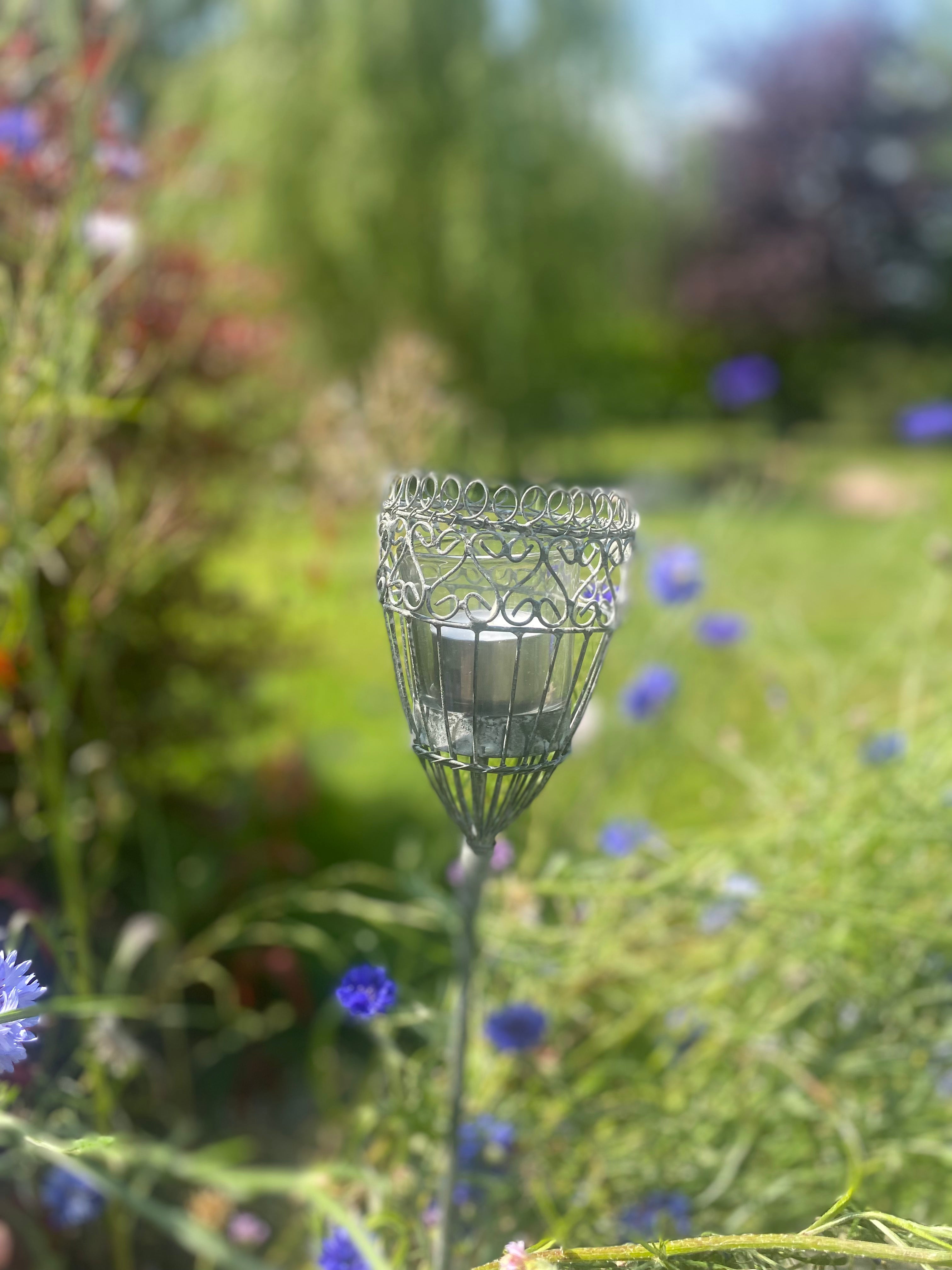 Antique grey French candle spear in garden setting with wild flowers around it