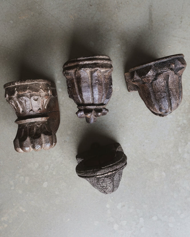 Four carved teak candle holders on a concrete surface