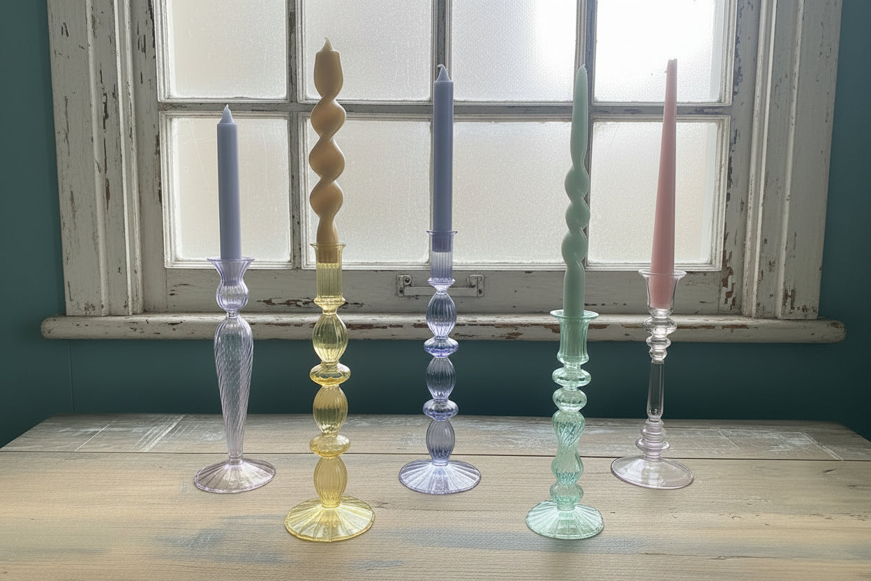 Group of coloured glass cande holders on wood table against old sash window